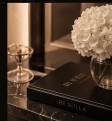 Still life of the Be Sulla branded book and orchid stems on a marble console